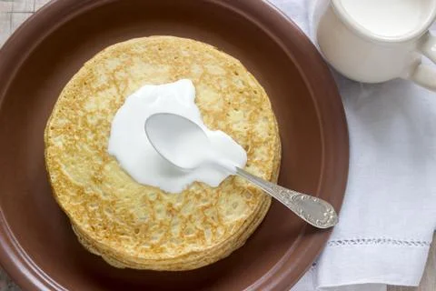 Stack of Russian pancakes with sour cream - blini on a plate on wooden table. Stock Photos