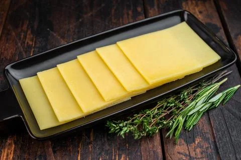 Stack of semi hard yellow cheese slices arranged on black tray, dairy ingre.. Stock Photos