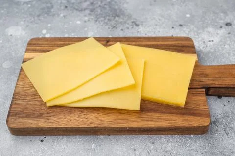 Stack of semi hard yellow cheese slices on rustic wooden cutting board, cop.. Stock Photos