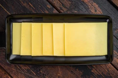 Stack of semi hard yellow cheese slices arranged on black tray, dairy ingre.. Stock Photos