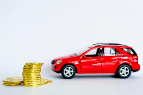 A stack of shiny yellow coins on a background of red car on a light gray back Foto stock