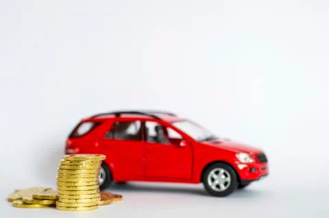A stack of shiny yellow coins on a background of red car on a light gray back Stock Photos