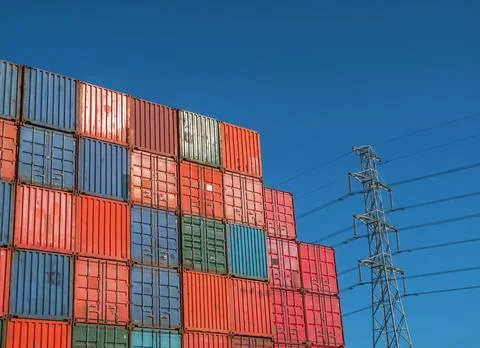 Stack of shipping containers with electricity pylon in background Stock Photos