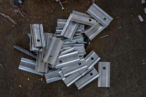 Stack of silver metal brackets with holes lying on rough soil background, rep Stock Photos