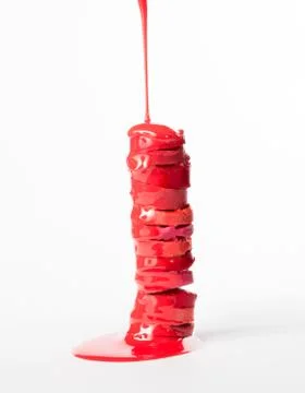 Stack of sliced moisturizing lipsticks with red paint, pouring on them Stock Photos