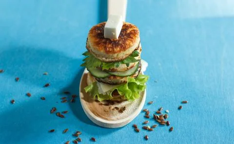 A stack of small pancakes with lettuce and cheese on a wooden spoon, blue Foto stock
