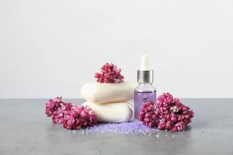 Stack of soap bars, sea salt, essential oil and lilac flowers on grey table.. Stock Photos