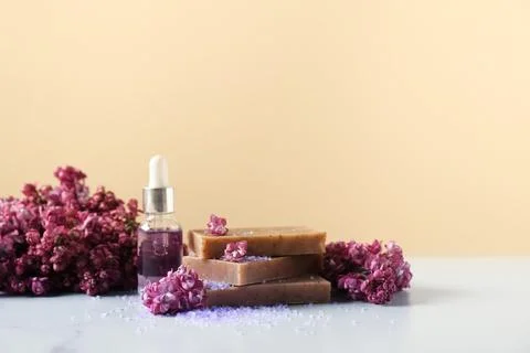 Stack of soap bars, sea salt, essential oil and lilac flowers on white tabl.. Stock Photos
