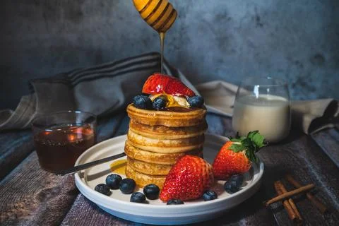 A stack of soft pancakes with pouring honey, fresh blueberry and strawberry a Stock Photos