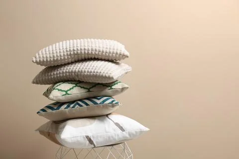 Stack of soft pillows on small table near beige wall. Space for text Foto stock