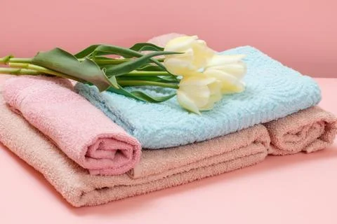 Stack of soft terry towels with tulips on a pink background. Stock Photos