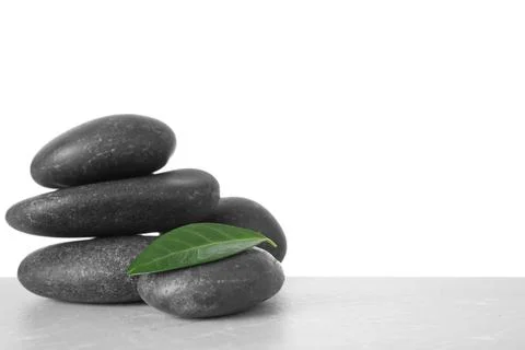 Stack of spa stones and green leaf on table against white background. Space f 写真素材