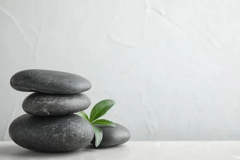 Stack of spa stones and green leaves on grey table, space for text 스톡 사진