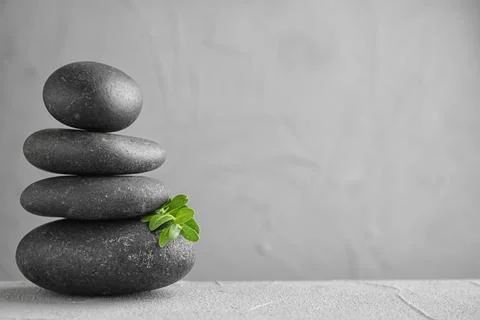 Stack of spa stones and green leaves on grey table, space for text 스톡 사진