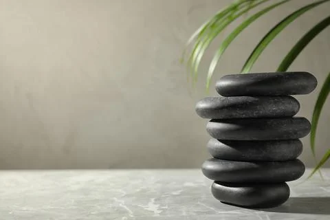 Stack of spa stones and palm leaf on grey table, space for text Stockfoto's