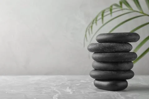 Stack of spa stones and palm leaf on grey table, space for text Foto stock