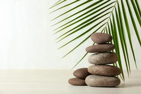 Stack of spa stones and palm leaf on table against white background, space fo 스톡 사진