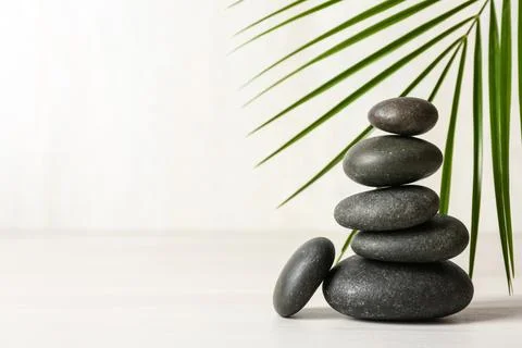 Stack of spa stones and palm leaf on table against white background, space fo 스톡 사진