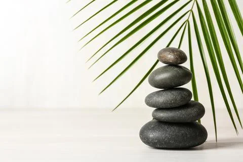 Stack of spa stones and palm leaf on table against white background, space fo 스톡 사진