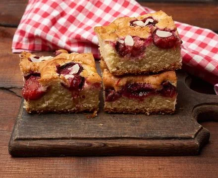Stack of square baked sponge cake slices with plums on wooden kitchen boar... Stock Photos