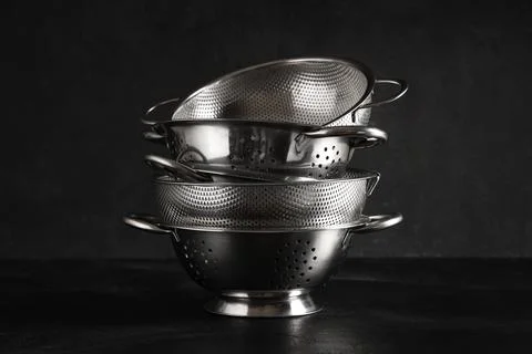 Stack of stainless steel kitchen colanders and strainers on a dark background Fotos de archivo