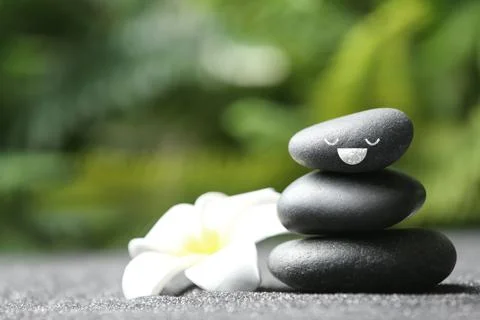 Stack of stones with drawn happy face and flower on grey table outdoors, spac Stockfoto's