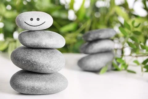 Stack of stones with drawn happy face on white table, space for text. Be in h 스톡 사진