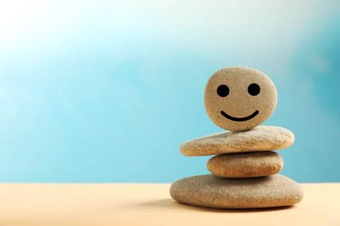 Stack of stones with drawn happy face on beige table against light blue backg 스톡 사진