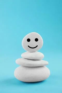 Stack of stones with drawn happy face on light blue background. Zen concept Foto stock
