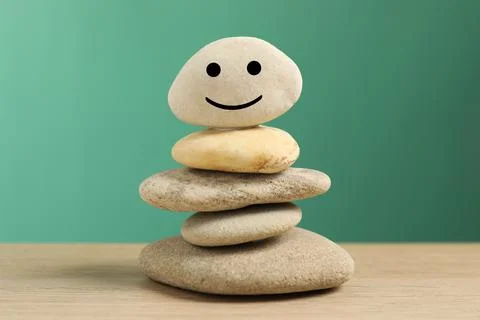 Stack of stones with drawn happy face on table against turquoise background,  Stockfoto's