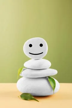 Stack of stones with drawn happy face and leaves on beige table against light Stock Photos