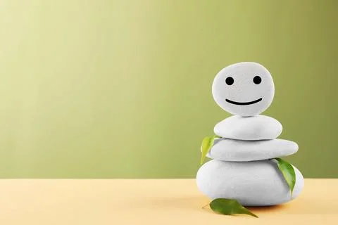 Stack of stones with drawn happy face and leaves on beige table against lig.. Foto stock