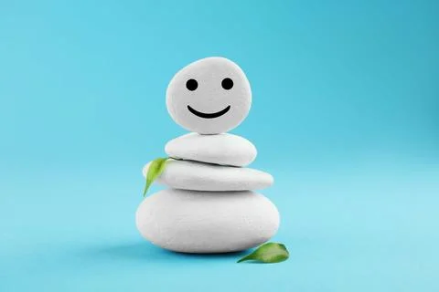 Stack of stones with drawn happy face and green leaves on light blue backgr.. Foto stock