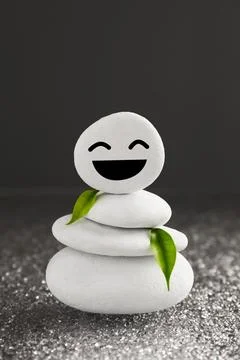 Stack of stones with drawn happy face and green leaves on grey background. .. 스톡 사진
