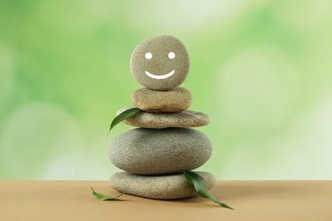 Stack of stones with drawn happy face and green leaves on table against blu.. 写真素材