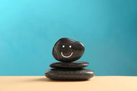 Stack of stones with drawn happy face on beige table against light blue bac.. Stock Photos
