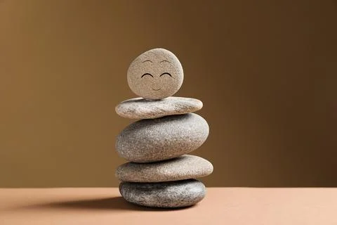 Stack of stones with drawn happy face on table against dark beige backgroun.. 스톡 사진