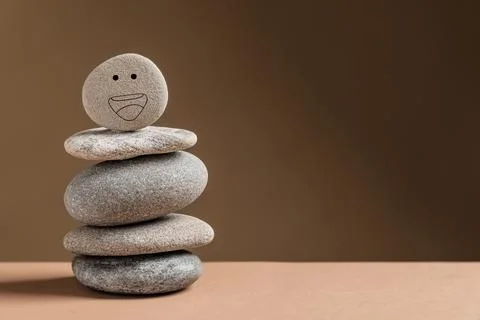 Stack of stones with drawn happy face on table against dark beige backgroun.. Stock Photos
