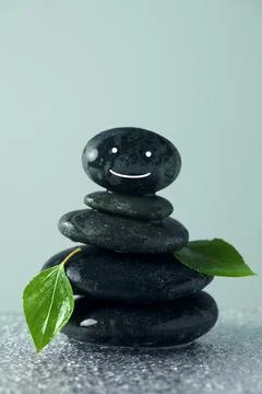 Stack of stones with drawn happy face, green leaves and water drops on tabl.. 库存照片