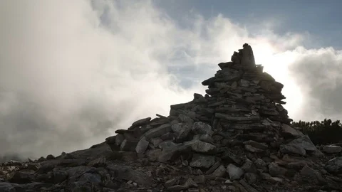Stack of stones on mountain top on background of rapidly running clouds on 스톡 동영상 77572122