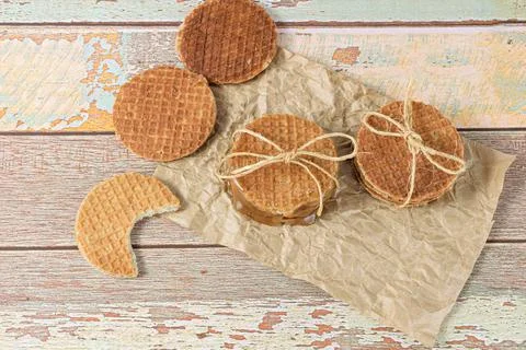 Stack stroopwafels on brown paper, next to another biscuit with a bite. Stock Photos