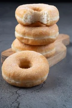 Stack of sugar ring donuts on a wooden board with top one bitten Stock Photos