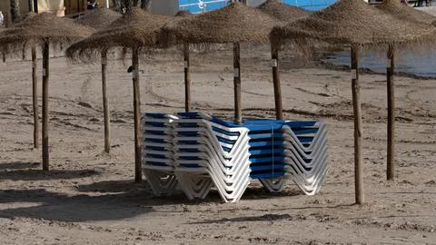 Stack of sun loungers under straw umbrellas on sandy beach Stock Photos