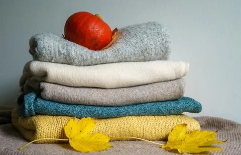 A stack of sweaters, a pumpkin and yellow maple leaves on a knitted blanket Foto stock
