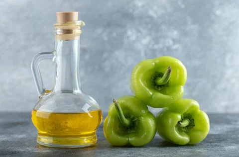 Stack of sweet peppers with bottle of oil on grey background. Close up photo Foto stock