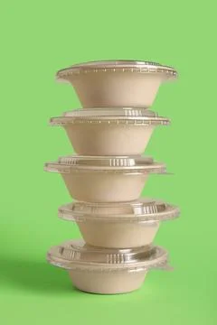 Stack of takeaway food containers with plastic lids on green background Stock Photos