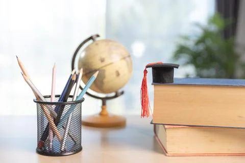 Stack of textbooks with graduation cap and red tassel beside pencil holder .. Stock-Fotos