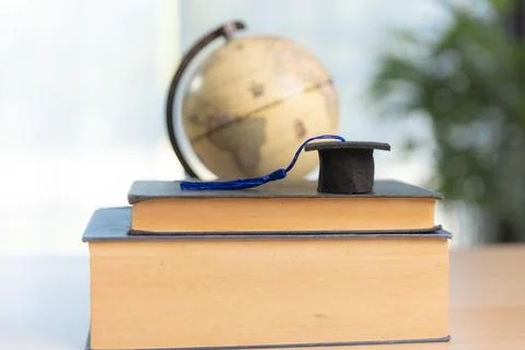 Stack of textbooks with graduation cap and red tassel beside pencil holder .. Stock Photos
