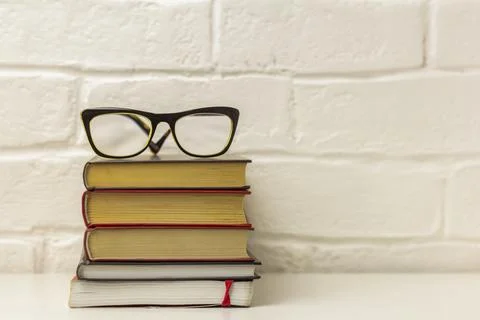 A stack of thick hardcover books and correction glasses on the table.Fiction  Stock Photos