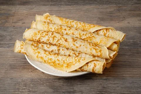 Stack of thin crepes on a white plate placed on a wooden table Stock Photos